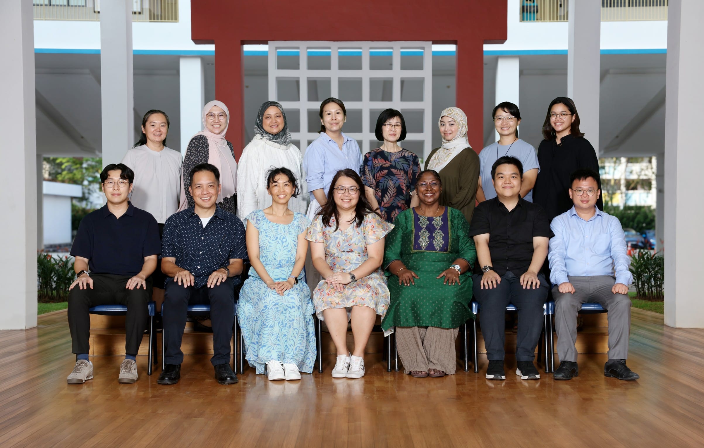 A group of about 14 adults posing for a formal photo in two rows inside a covered corridor.